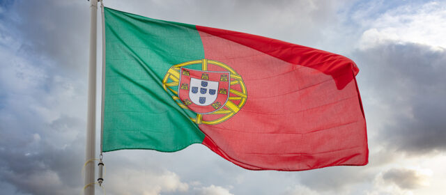 Portugal sign symbol. Portuguese Republic national flag on a pole waving against cloudy sky background.