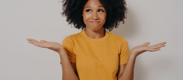 Young african woman standing with clueless and funny confused expression with arms and hands raised